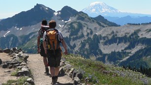 Hikers walk along a trail with a view of rocky mountain and Mount Adams.