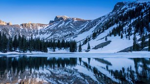 Snow covered mountain with pine trees reflected in lake