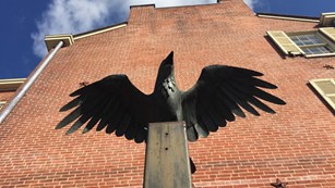 Statue of a raven spreading its wings outside of a brick building