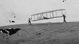 Black and white photo of three men flying gliding airplane