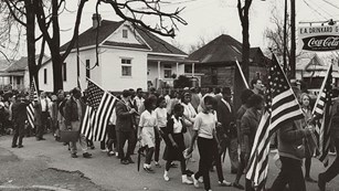 Black and white photo of marches carrying American flags.