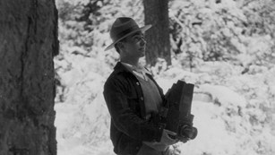 Black and white historic photo of George Wright holding a camera in the woods