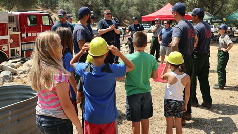 Firefighters and kids learn play a  bucket brigade game at a festival.