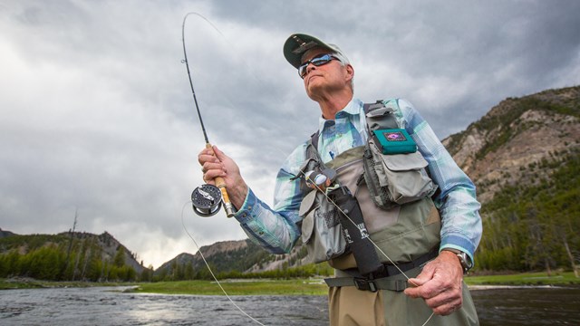 close up of man fly fishing with rod in mid air