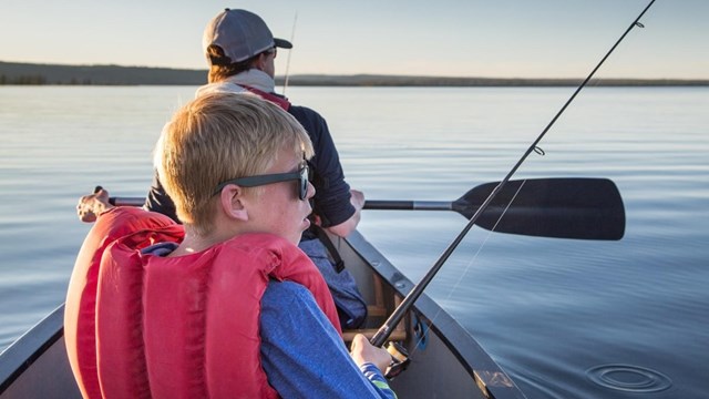 Child fishes off of canoe with spin rod in hand. 