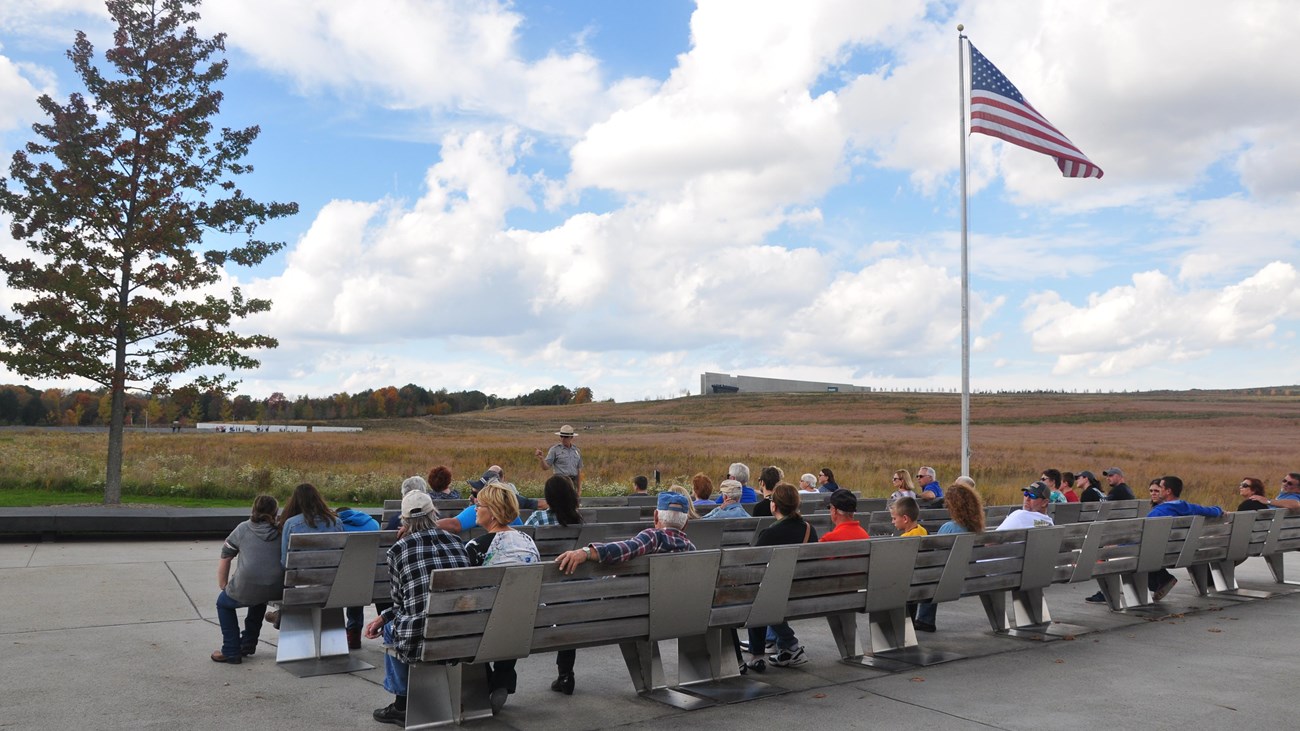 Group of people on benches at flag pole.