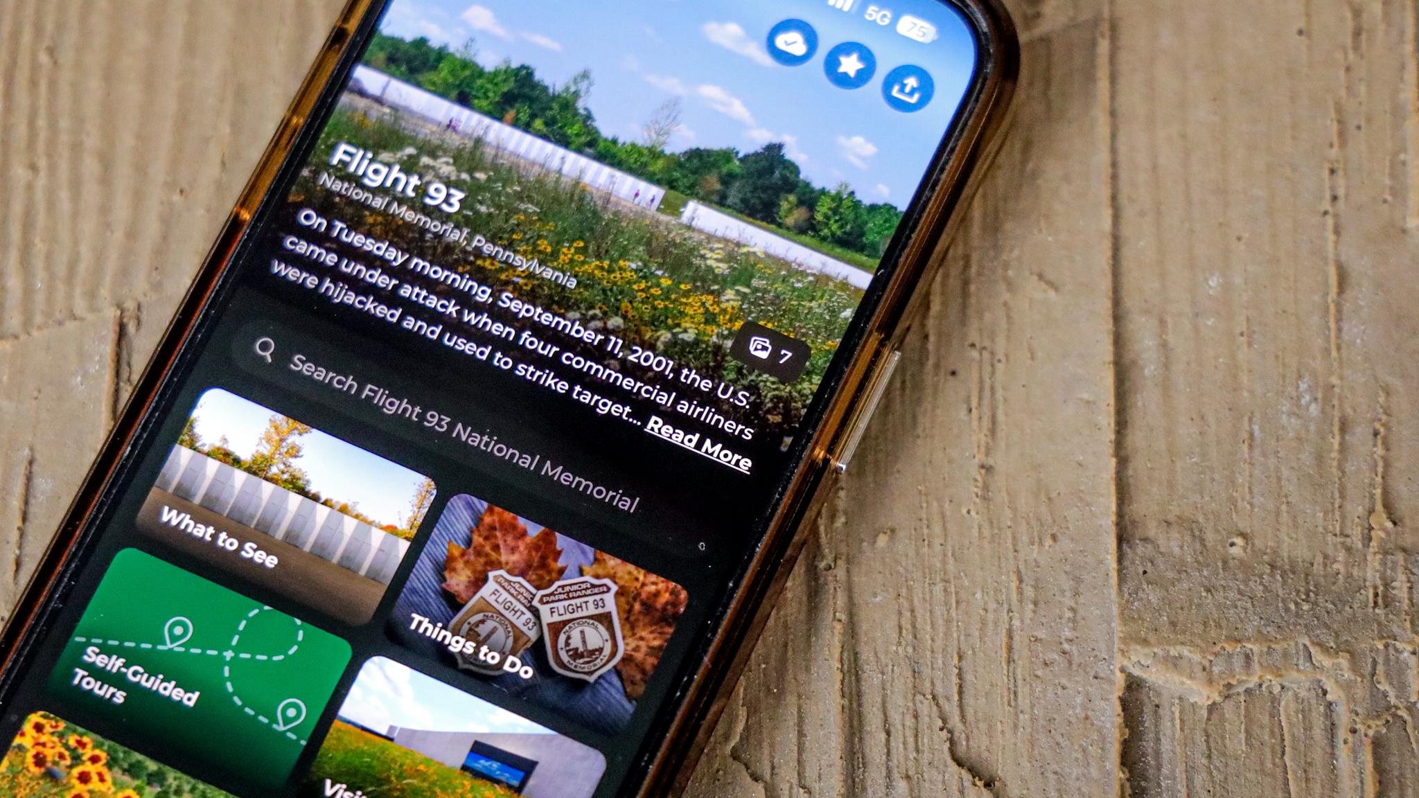 A phone sitting on a textured surface. On the screen is the NPS App. 