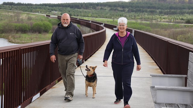 Visitor walking a dog on the wetlands bridge.