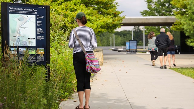 A visitor reading the Memorial Plaza entrance wayside.