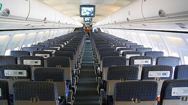 An interior image of a plane with airfones on the seatbacks 