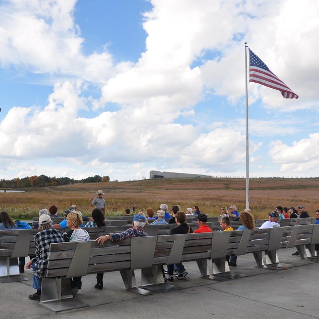 Group of people on benches at flag pole.
