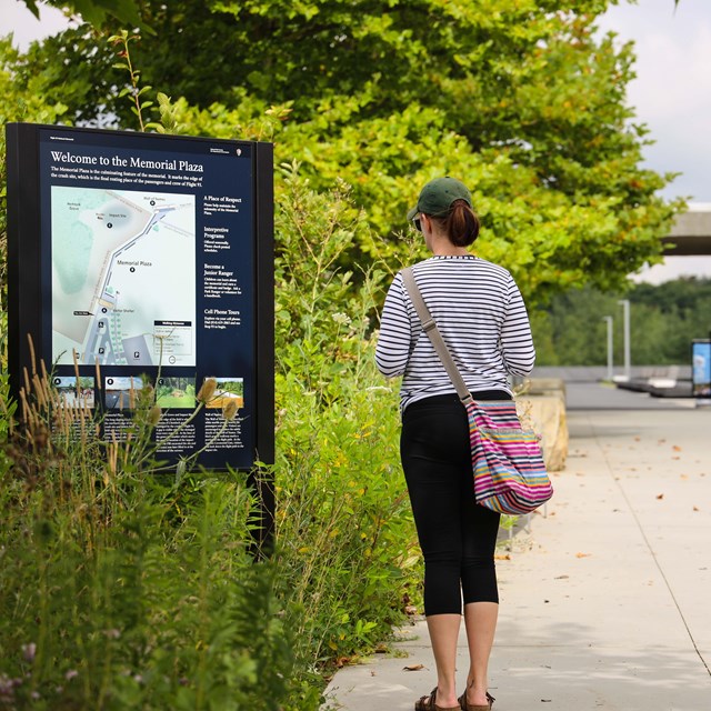 A visitor reading the Memorial Plaza entrance wayside.