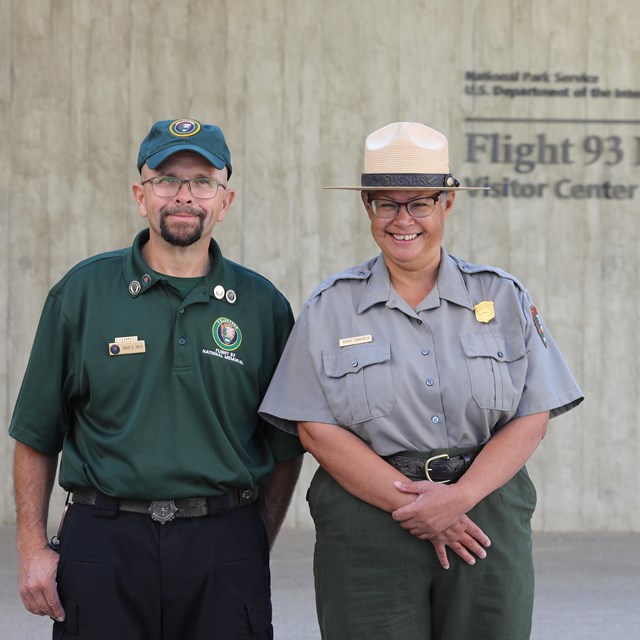 Volunteer and ranger in uniform standing at the entrance of the visitor center.
