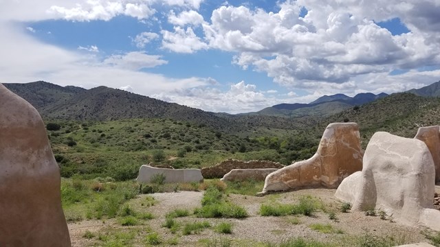 Crumbled white walls stand out against a background of green and mountains.