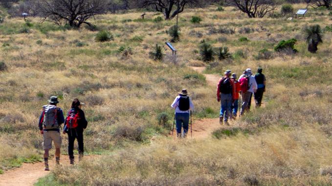 People hiking a dirt trail with mountains in the background.