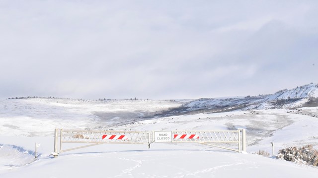 A gate with a sign saying road closed blocks Fossil Butte's scenic drive which is covered in snow.