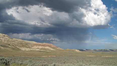 Cloudy sky and rain falling on the butte and the sagebrush lowlands.