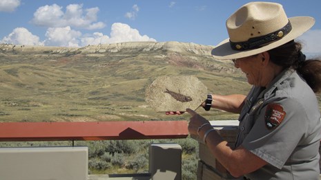 A ranger standing in front of Fossil Butte holding a fossil fish and pointing at it