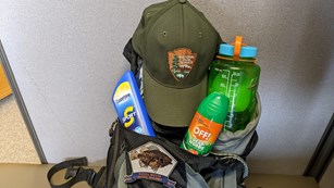 A backpack with a Fossil Butte patch and a water bottle, sunscreen, bug spray, and NPS ball cap.
