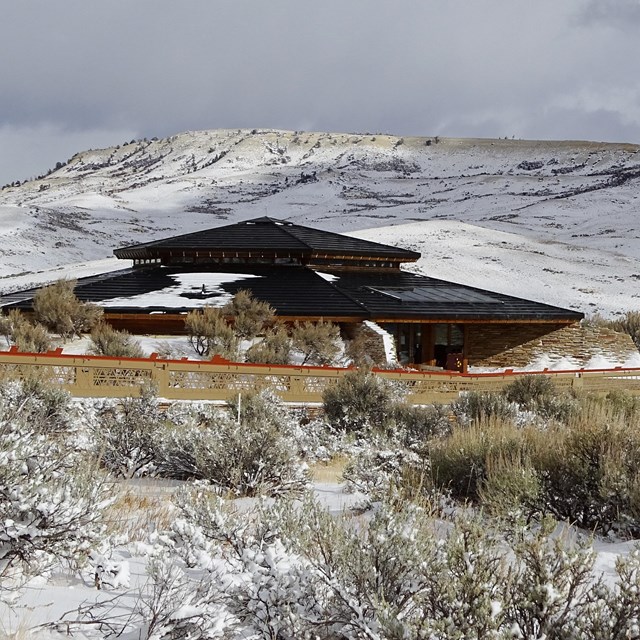 The visitor center with sagebrush in front and the snow-covered butte behind.