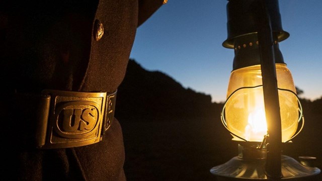 A close-up of a mans belt and lit lantern. 