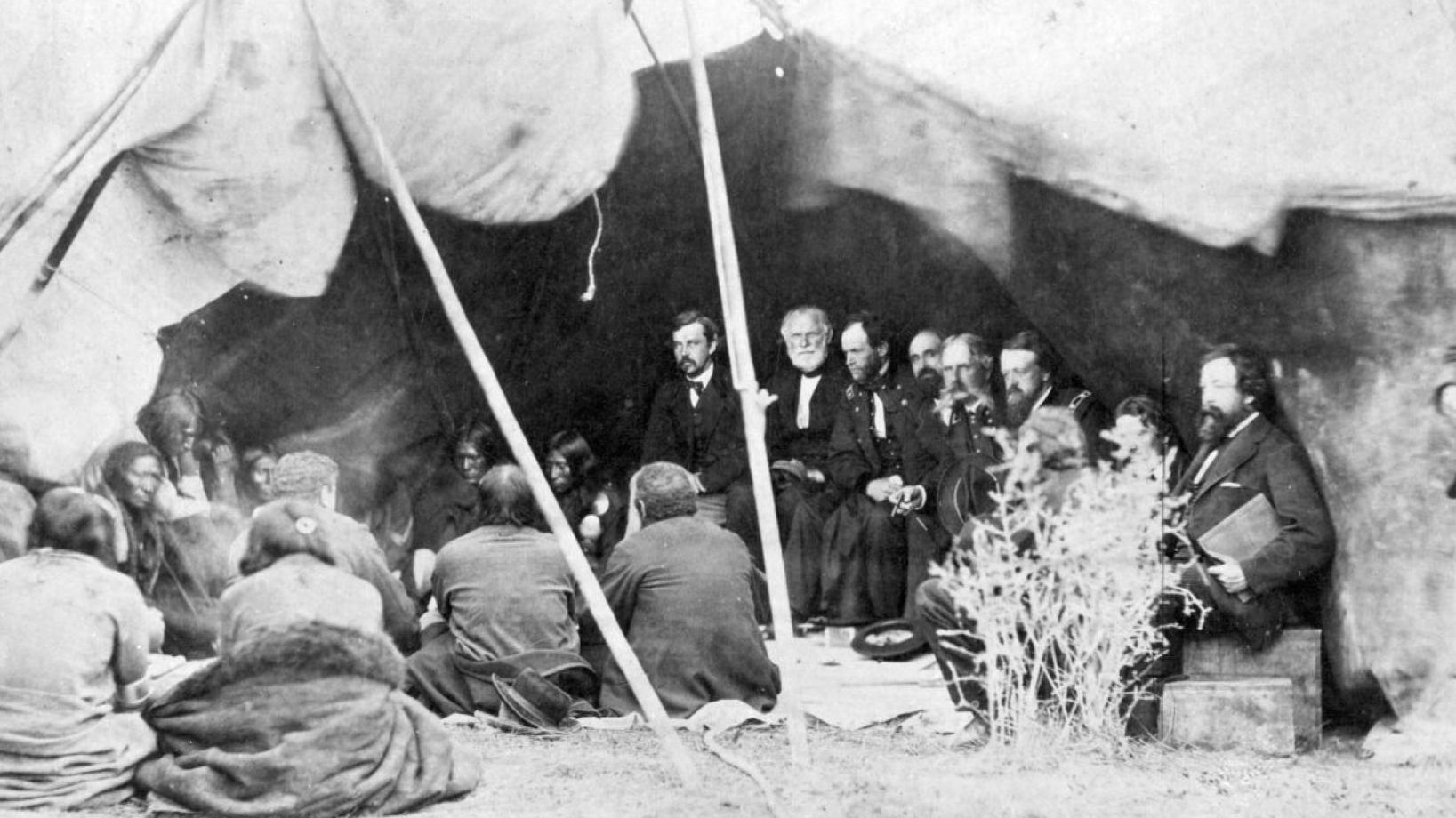 A diverse group of people seated near a tent, participating in a social gathering. 