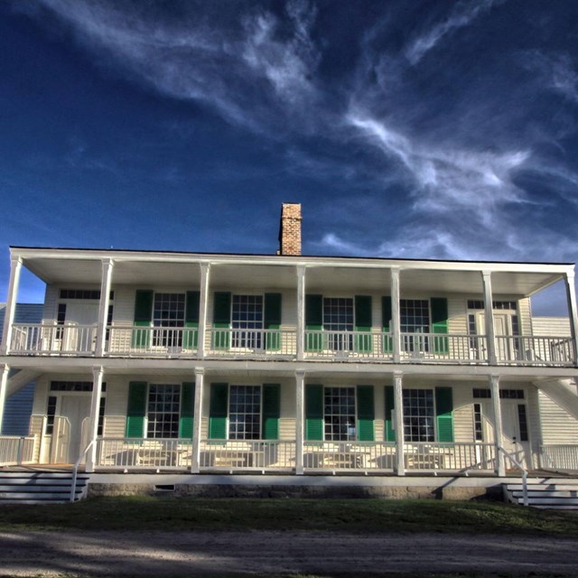 Large white structure with two stories. Made out of wood with green trim.