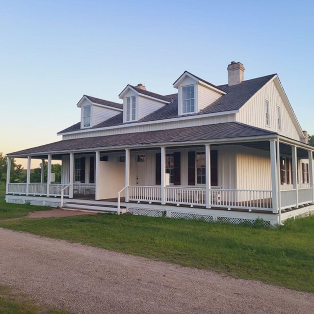 White wood building that is two stories tall, with a gray wrap around porch.  