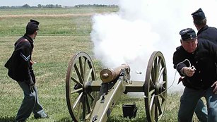Men dressed in 19th century U.S. Army uniforms firing a cannon.