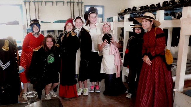 Young women dressed in 19th century women's clothing in the fort barracks.