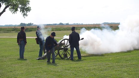 Re-enactors in 19th Century U.S. Army uniforms fire a cannon.
