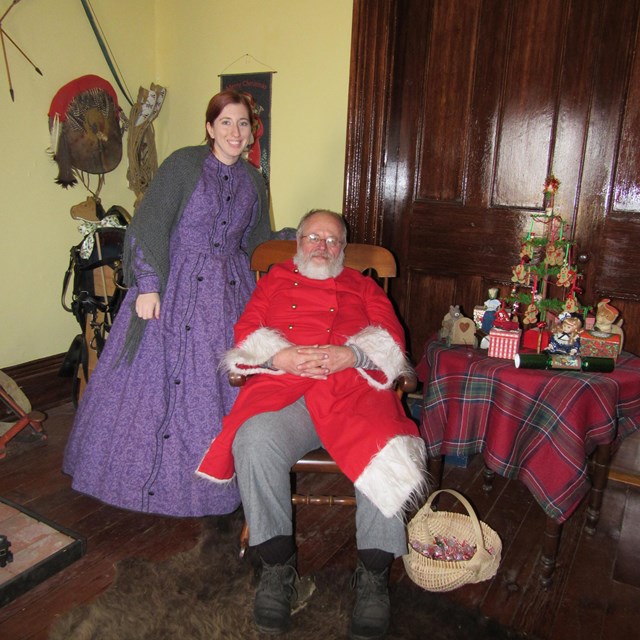 Santa and woman in hooped skirt in historic building.