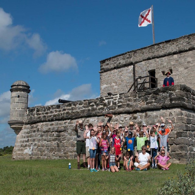 Group of students in front of fort with ranger. 