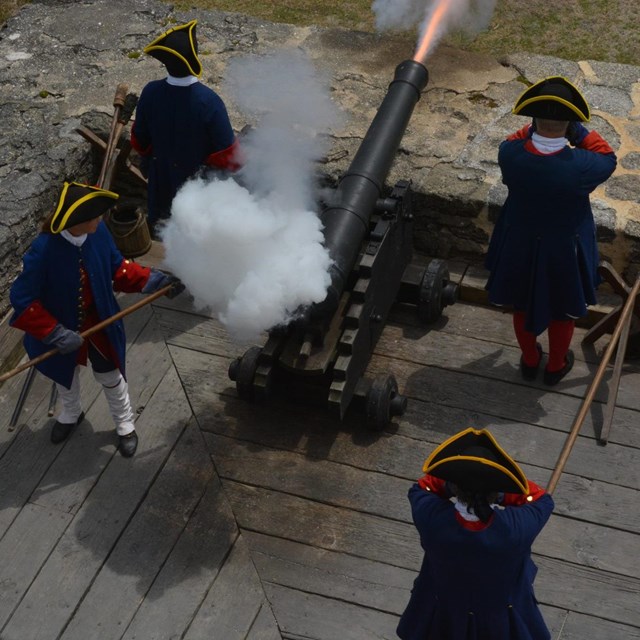 Cannon being fired surrounded by four soldiers. 