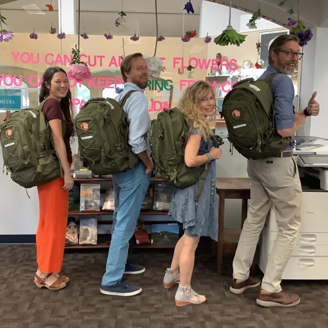 Four people wearing green NPS backpacks in the library. 