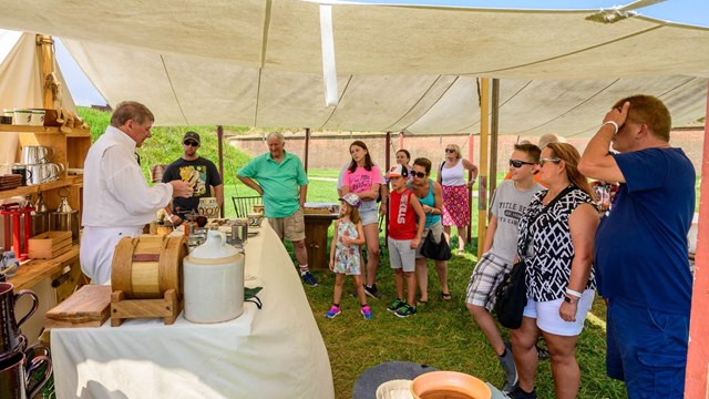 A living history volunteer giving a demonstration under a tent.