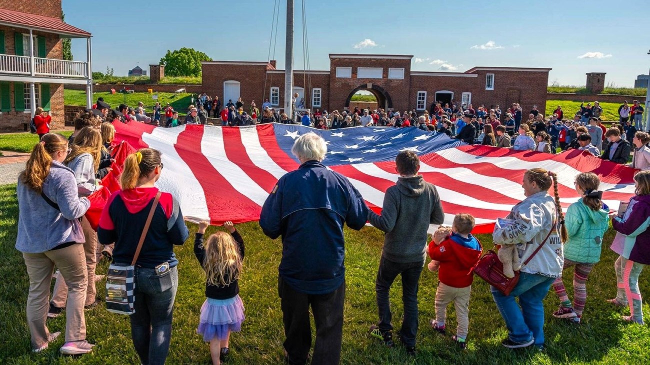 Large group of visitors assisting with folding a large American flag