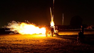 A cannon being fired at night with the fort in the background.