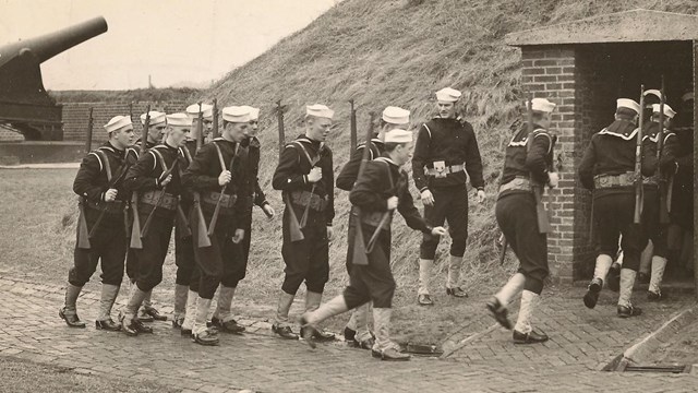 A black and white photograph of coast guards men in WWII enter Fort McHenry.