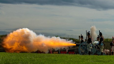 A picture of living historians firing a cannon while wearing corps of artillery uniforms.