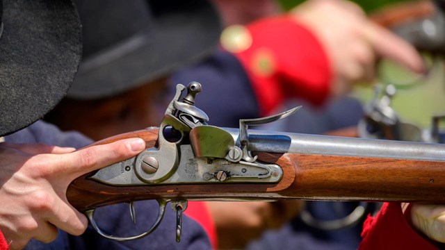 A close up image of living historians firing muskets while wearing militia uniforms.