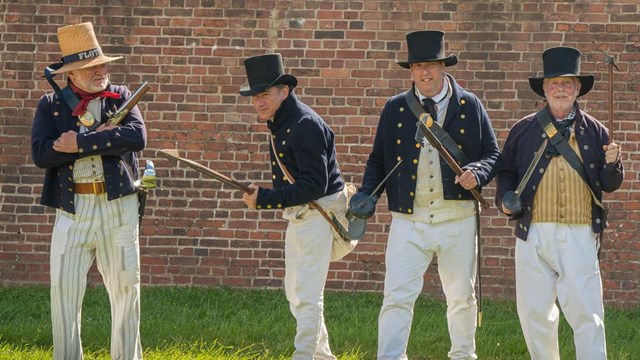 Living historians dressed as flotilla sailors show off weapons that sailors would have used.