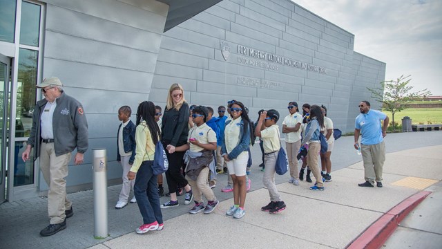 A school group walking into the visitor center with a volunteer.