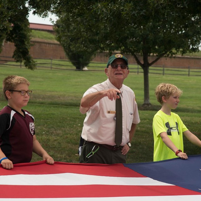 An elderly man talking about the USA flag, to a group of young visitors.
