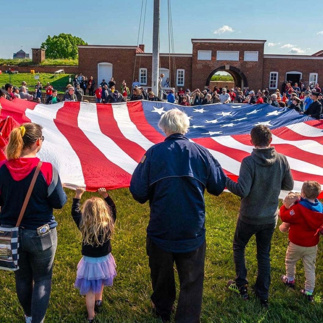 Large group of visitors assisting with folding a large American flag