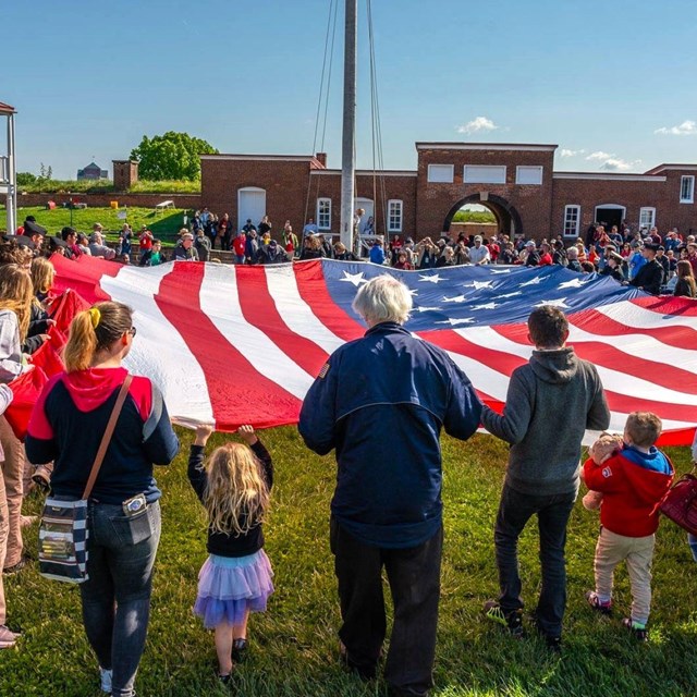 Large group of visitors assisting with folding a large American flag