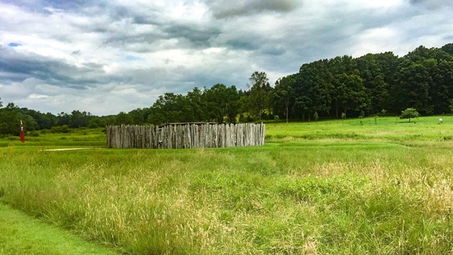 A wooden stockade and earthworks in a meadow.