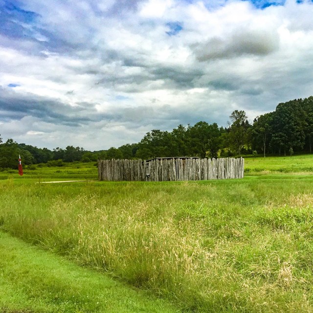 A wooden stockade and earthworks in a meadow.