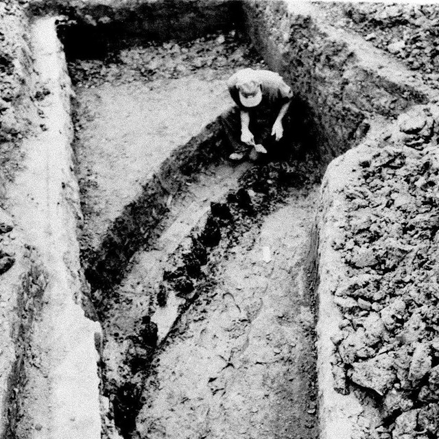 A man in a ditch looking at the remains of the original Fort Necessity stockade