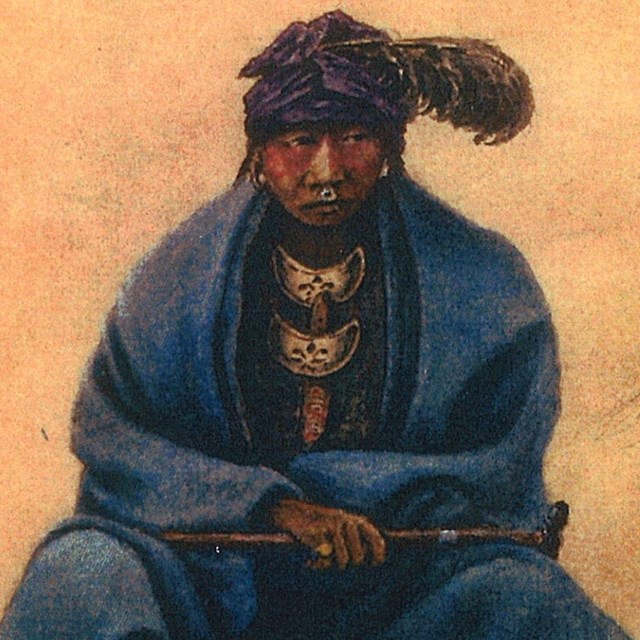 A seated American Indian wear a blue blanket around his shoulders